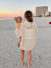 Load image into Gallery viewer, A woman standing on a sandy beach at sunset, holding a young child. The woman is wearing an oversized cream hoodie with the text 'KINDA CHIC TO RAISE TINY HUMANS' printed in white on the back.