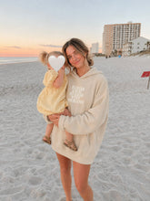 Load image into Gallery viewer, A woman and a toddler standing on a sandy beach at sunset. The woman wears a cream-colored oversized hoodie with the text 'KINDA CHIC TO RAISE TINY HUMANS' printed on the front.
